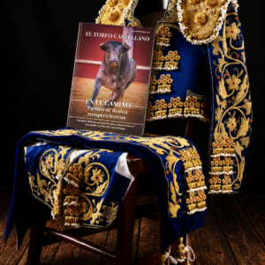 Ejemplar de El Toreo Castellano nº 65 apoyado sobre una silla junto a un traje de luces azul y oro.