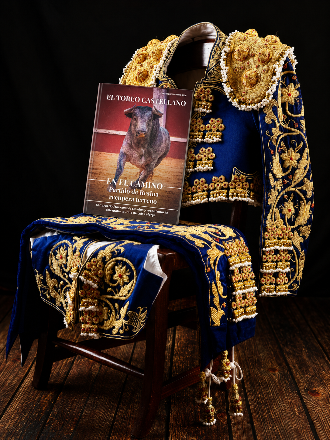 Ejemplar de El Toreo Castellano nº 65 apoyado sobre una silla junto a un traje de luces azul y oro.